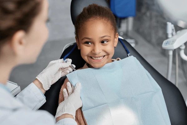 Child smiling in a dental chair during a consultation, with a dentist preparing for a procedure, emphasizing a positive dental experience related to All-on-4 dental implants.